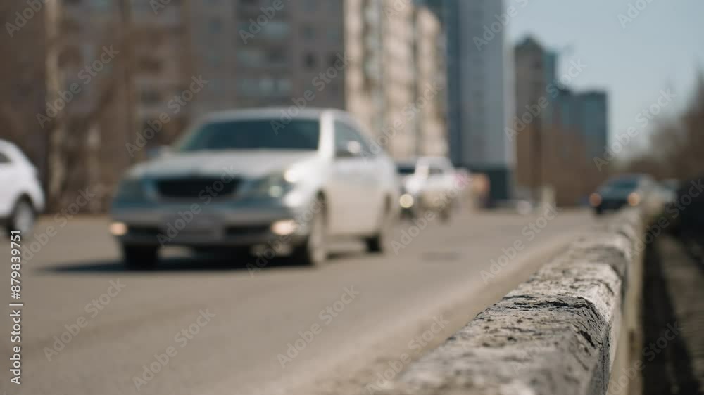 Close view of a city road with cars in motion in the background, the focus is on the weathered road barrier and cars in motion