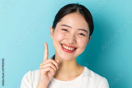 Skincare with pretty Asian Korean beauty woman pointing finger short hair, makeup glowing face and healthy facial skin portrait smile on isolated blue background.