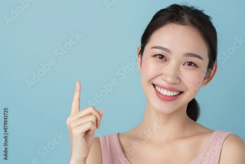 Skincare with pretty Asian Korean beauty woman pointing finger short hair, makeup glowing face and healthy facial skin portrait smile on isolated blue background.