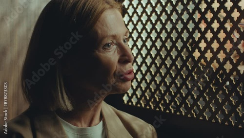 Senior female penitent telling about her sins to priest through latticed screen of confessional in church
