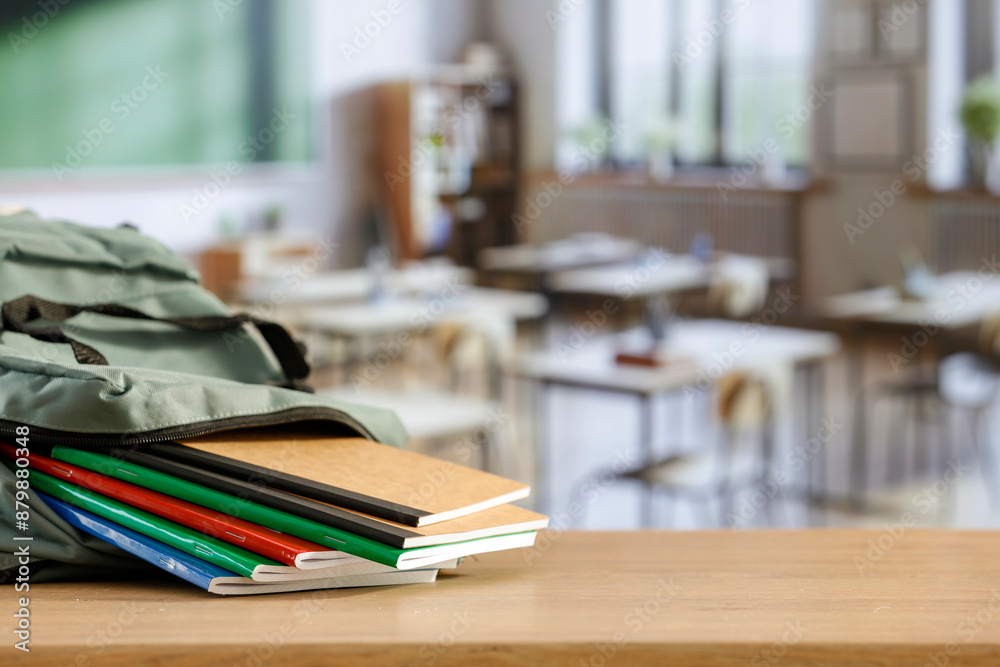 Back to school concept. Wooden desk top with backpack and apple and school stuff with blurred classroom backround Back to school concept. Wooden desk top with backpack and apple and school stuff with blurred classroom backround