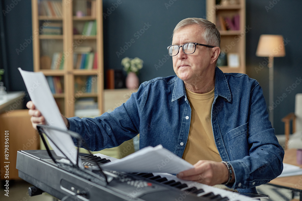 Portrait of senior man playing piano and reading sheet music while enjoying creative hobby in retirement Portrait of senior man playing piano and reading sheet music while enjoying creative hobby in retirement
