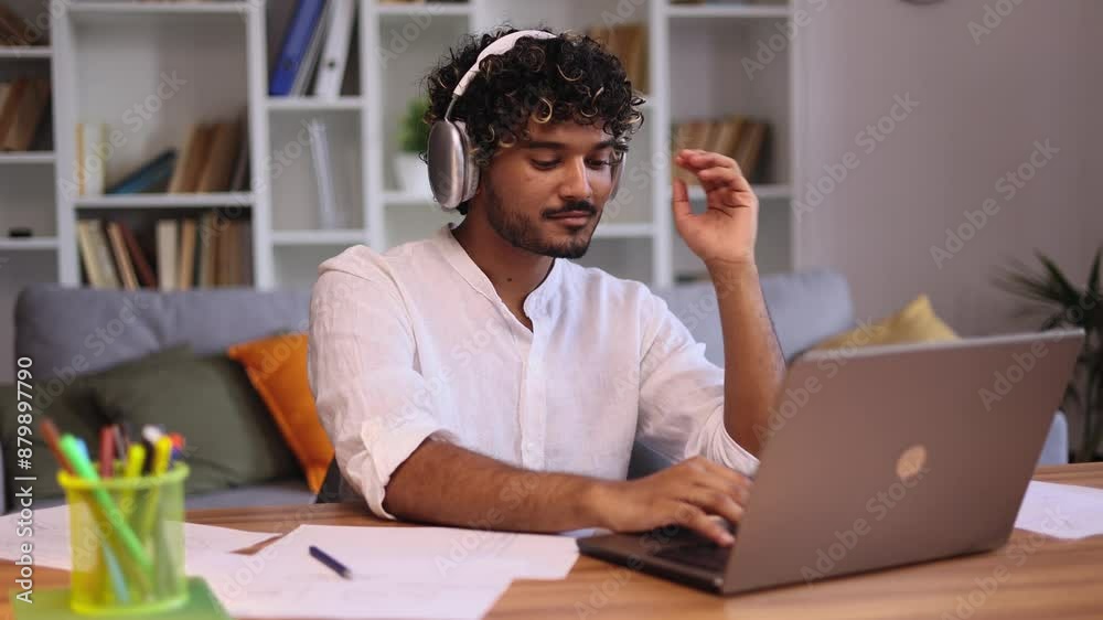 Portrait of handsome young man freelancer with headphones listening music while having distance remote work typing browsing scrolling products in internet online store on laptop computer at home
