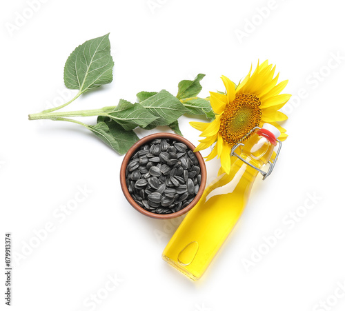 Bottle of sunflower oil and bowl with seeds on white background