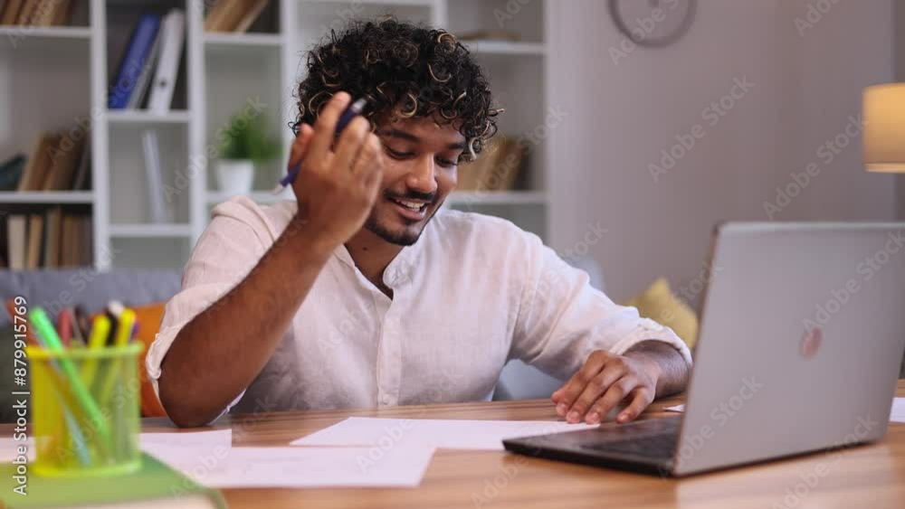 Busy indian guy preparing for exam at university studying at home workplace Positive student make notes while looking at laptop computer talking with teacher lesson indoors Distance remote education	