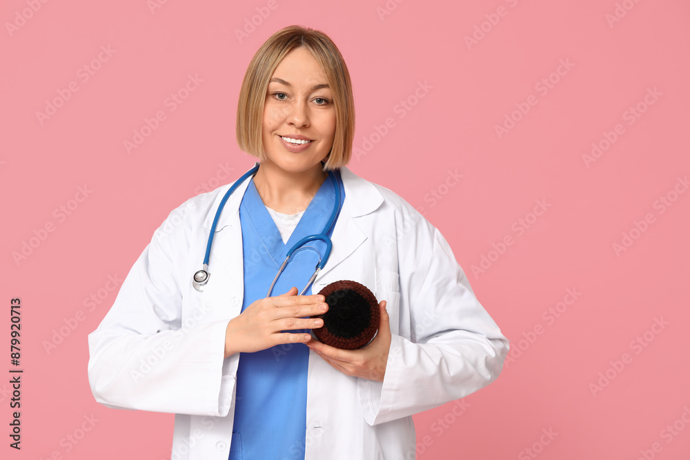 Mature happy female doctor with stethoscope and knitted model of breast on pink background. Breast feeding concept Mature happy female doctor with stethoscope and knitted model of breast on pink background. Breast feeding concept