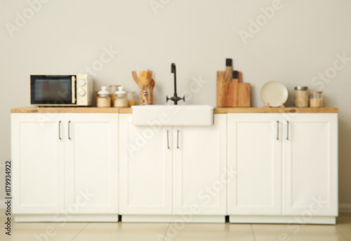 Stylish interior of kitchen with sink, white counters and microwave, blurred view