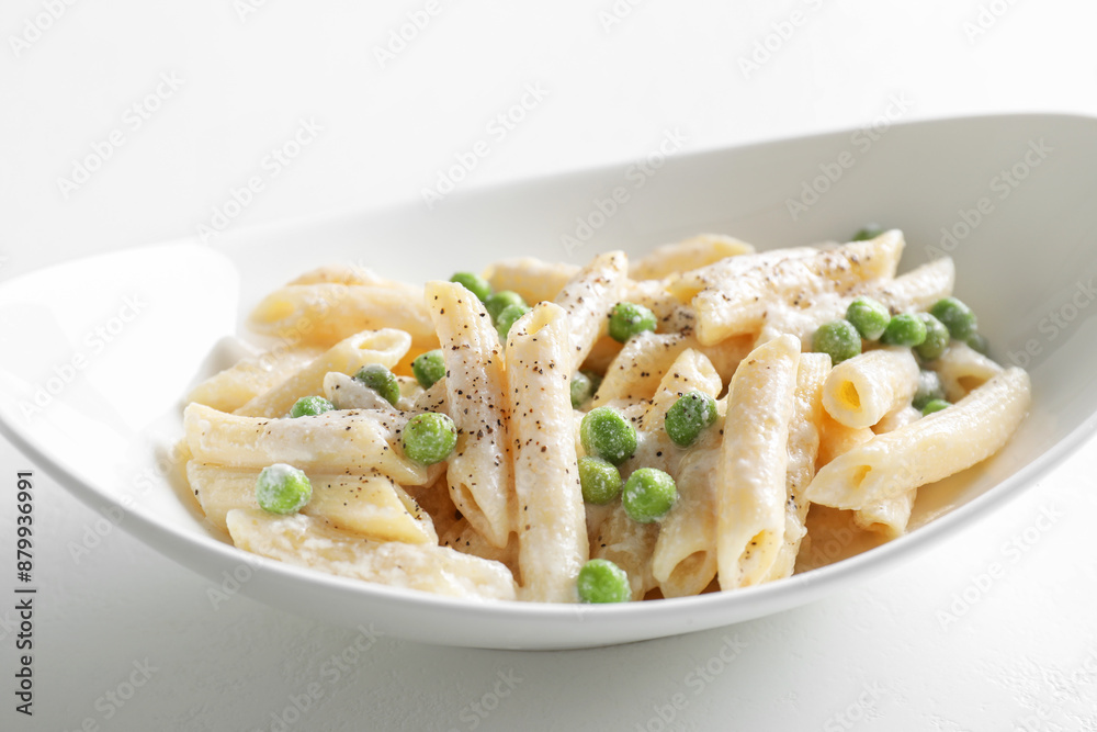Delicious pasta with green peas and creamy sauce in bowl on white table Delicious pasta with green peas and creamy sauce in bowl on white table