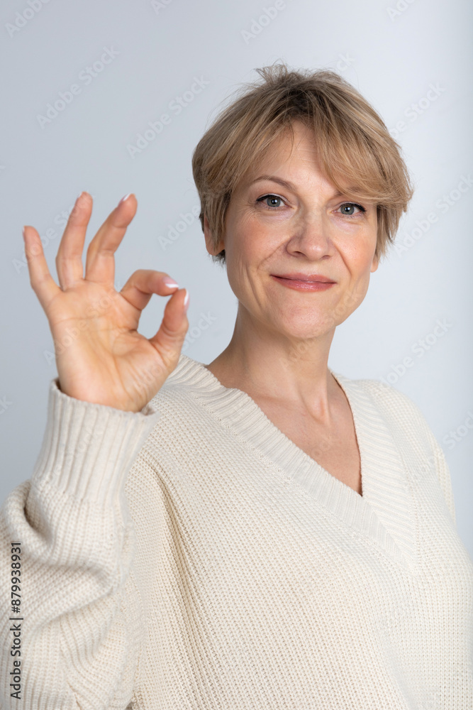 Portrait of emotional woman. Woman's hand gesturing good or sign OK on light grey background. Looking at camera. High quality photo Portrait of emotional woman. Woman's hand gesturing good or sign OK on light grey background. Looking at camera. High quality photo