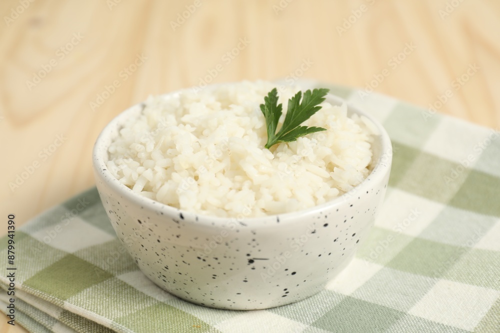 Delicious boiled rice in bowl and parsley on table, closeup