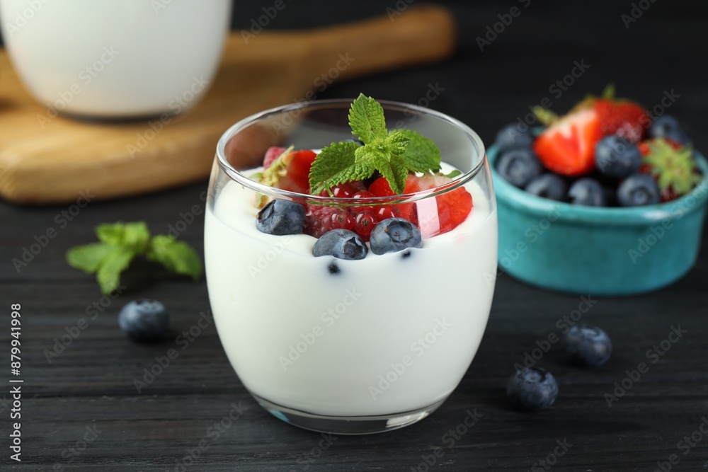 Tasty yogurt with fresh berries and mint in glass on black wooden table, closeup Tasty yogurt with fresh berries and mint in glass on black wooden table, closeup