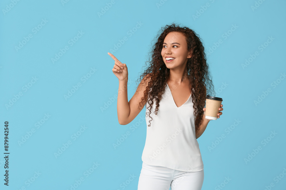 Happy young African-American woman with paper cup of coffee pointing at something on blue background Happy young African-American woman with paper cup of coffee pointing at something on blue background