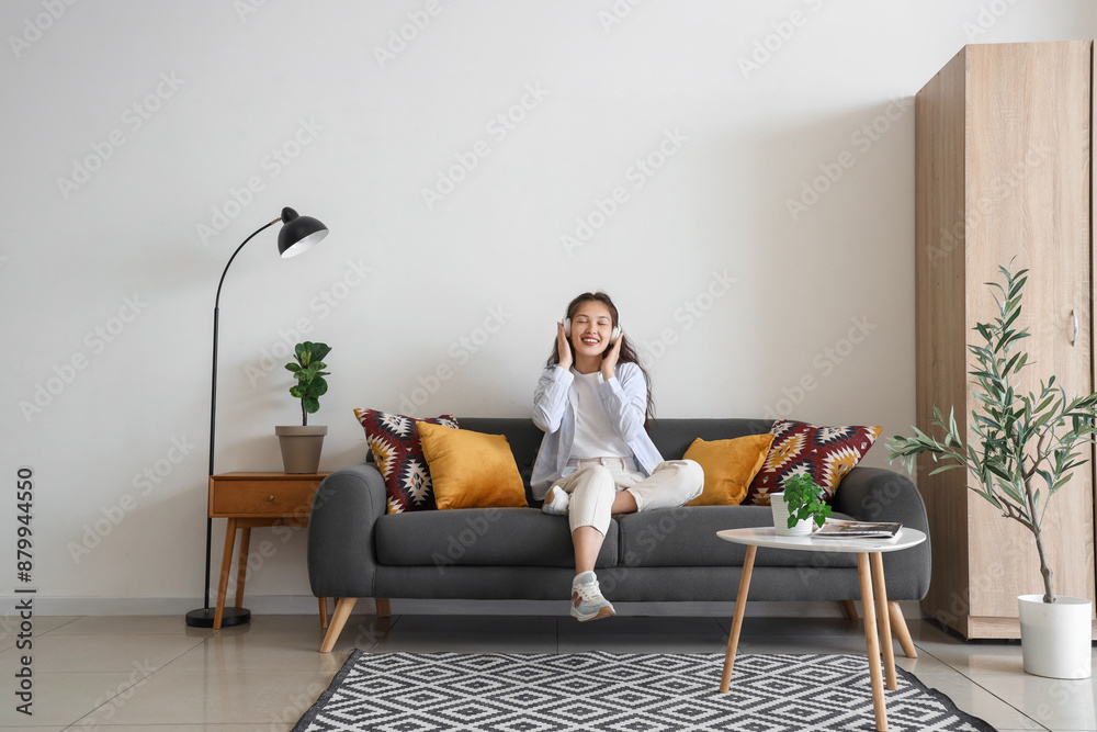 Obraz premium Young Asian woman in headphones sitting on black sofa at home