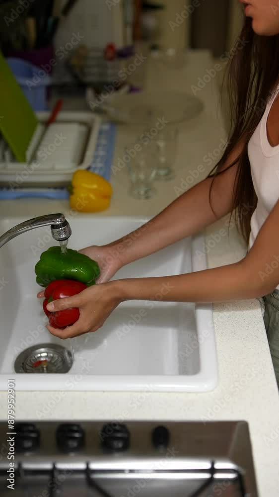 In the kitchen sink, a woman is washing bell peppers, preparing a nutritious meal In the kitchen sink, a woman is washing bell peppers, preparing a nutritious meal