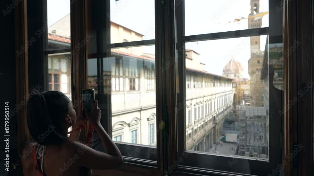 A woman is peacefully admiring the cityscape view from inside a historic building through a window A woman is peacefully admiring the cityscape view from inside a historic building through a window