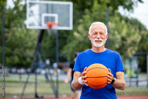 Senior man in sportswear holding ball on basketball court.