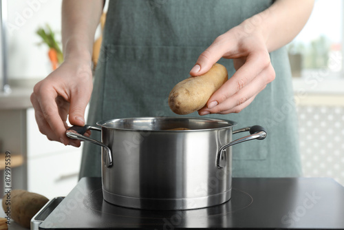 Woman putting potato into metal pot on stove, closeup