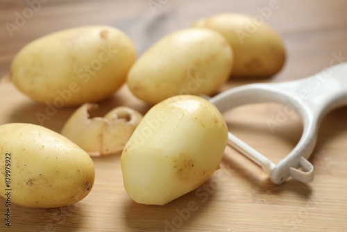 Fresh raw potatoes and peeler on wooden table, closeup