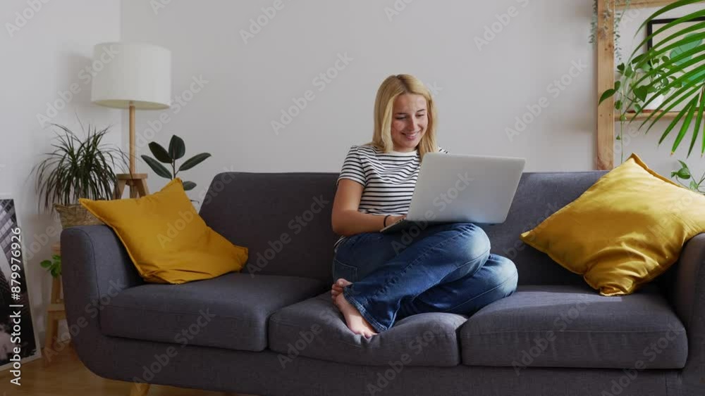 Young woman working on laptop computer while sitting on sofa in the living room. Millennial pretty student girl studying online. Young woman working on laptop computer while sitting on sofa in the living room. Millennial pretty student girl studying online.