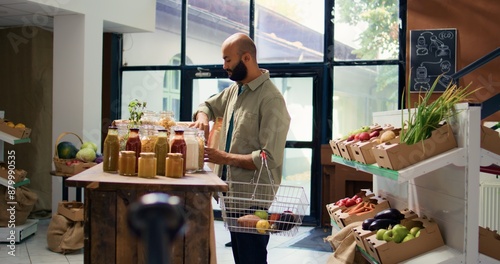 Young client shops at supermarket, supporting local vendors and choosing eco friendly fruits and vegetable from crates. Middle eastern person smells spices stored in nonpolluting jars.