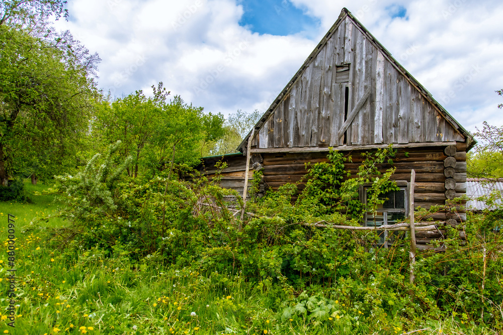The facade of an abandoned wooden house with windows. The old residential architecture is destroyed and abandoned. A log wall with windows and a roof. The facade of an abandoned wooden house with windows. The old residential architecture is destroyed and abandoned. A log wall with windows and a roof.