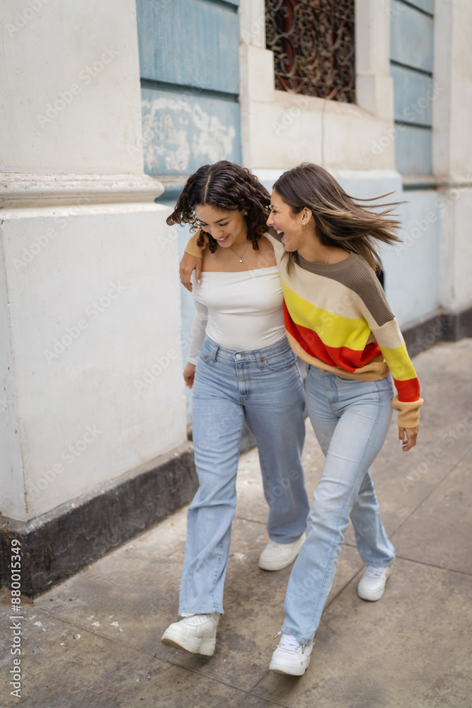 Two female friends walking down the street laughing together Two female friends walking down the street laughing together