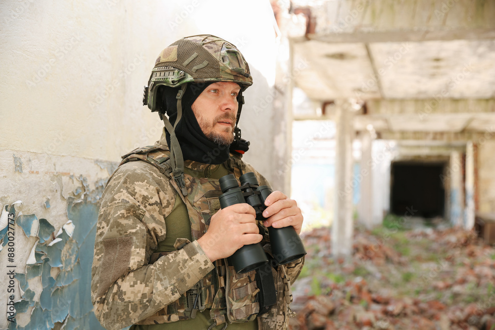 Fototapeta premium Military mission. Soldier in uniform with binoculars inside abandoned building
