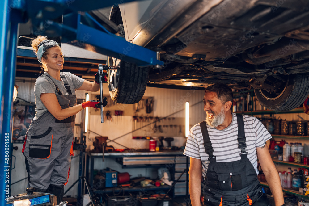 Smiling colleagues technicians standing at car repair shop and fixing car Smiling colleagues technicians standing at car repair shop and fixing car