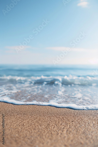 Close-up of gentle waves on a sandy beach with a clear blue sky, evoking tranquility and peace.