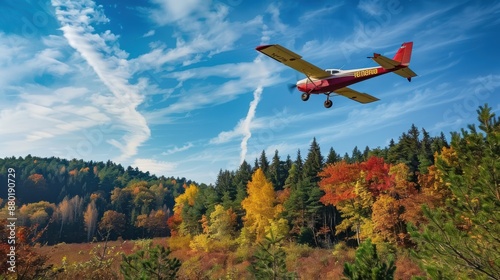 A small propeller plane flying over a dense, colorful forest during autumn
