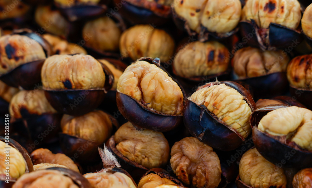 A close-up view of roasted chestnuts piled high at a market stall. The chestnuts are warm and inviting, with their shells slightly cracked open to reveal the soft, creamy interior. A close-up view of roasted chestnuts piled high at a market stall. The chestnuts are warm and inviting, with their shells slightly cracked open to reveal the soft, creamy interior.