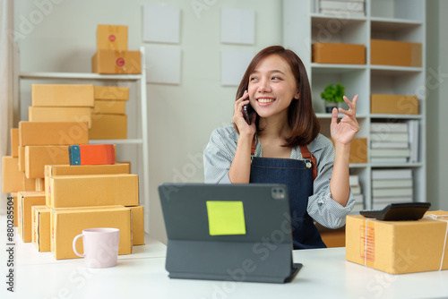 Small business startup, SME owner, female entrepreneur working on parcel boxes Receipt and check online orders via mobile phone in order to prepare boxes for sale to customers. Online SME concept.