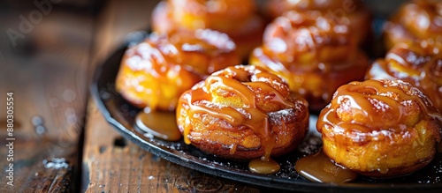 Close-up horizontal image of homemade pumpkin cinnabons drizzled with cane sugar caramel on a dark wooden table, with room for text or graphics in the shot. photo