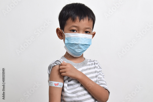 Asian boy using face mask with plaster bandage on his arm after vaccination. Vaccine injection. Child immunization. Health services for children. copy space