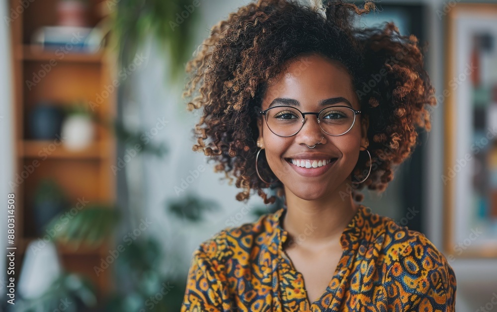 A woman with curly hair and glasses is smiling at the camera. She is wearing a colorful dress and has a nose piercing A woman with curly hair and glasses is smiling at the camera. She is wearing a colorful dress and has a nose piercing