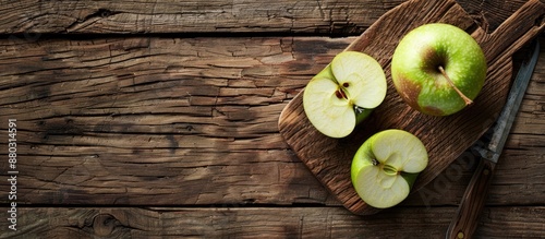 An image featuring a sliced green apple on a chopping board placed on a rustic wooden table with a lot of empty space for text or elements is displayed. photo