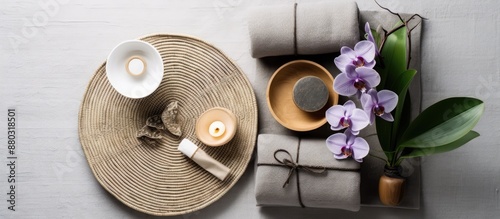 Flat lay arrangement featuring a bamboo mat, spa herbal pouches, an orchid-filled bowl on a grey surface, accompanied by space for text. photo