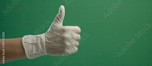 Protective glove being used in a thumbs-up hand gesture on a green background, conveying agreement and positivity, with copy space image. photo