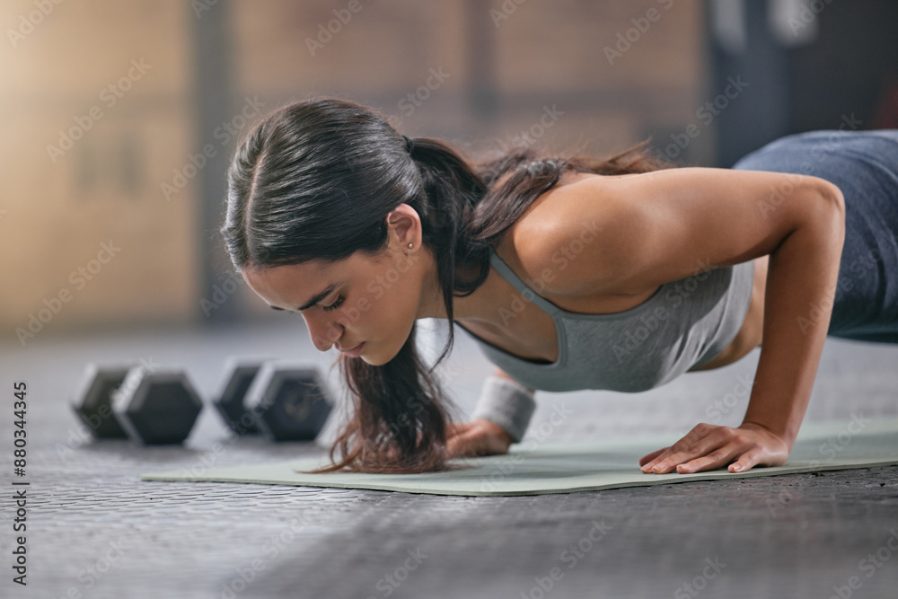 Fototapeta premium Gym, woman and serious with push ups for muscle or body building for wellness, wellbeing and self care. Female person, training centre and club with exercise or workout for fitness and strength