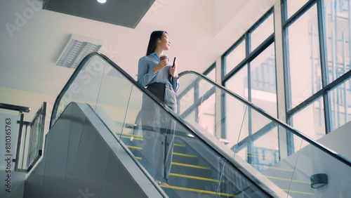 A business woman is walking down to escalator with a coffee cup in her hand