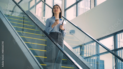 A business woman is walking down to escalator with a coffee cup in her hand