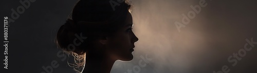 Silhouette of a woman with elegant hairstyle against a dark, smoky background, showcasing grace and mystery.