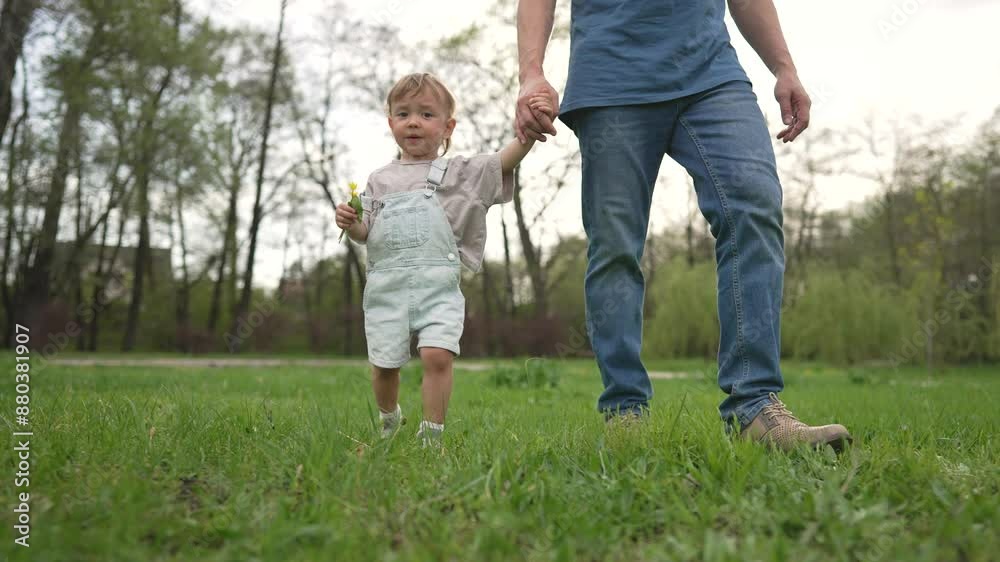 Dad walks with child holding hands in park. Family enjoys peaceful walk together as child explores nature. Family in park. Happy child holds flower while walking with dad. Child dad park outdoor fun. Dad walks with child holding hands in park. Family enjoys peaceful walk together as child explores nature. Family in park. Happy child holds flower while walking with dad. Child dad park outdoor fun.