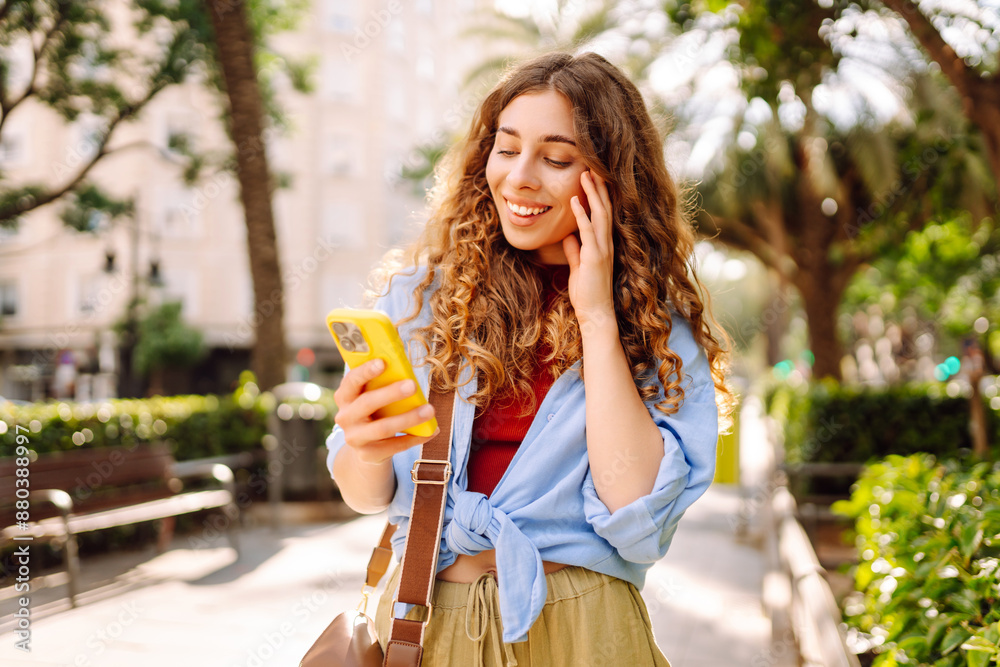 Obraz premium Woman traveler with a mobile phone on the street city. Young Woman texting, browsing, using her smartphone on a warm sunny day. Business, technology, blogging, communication concept.