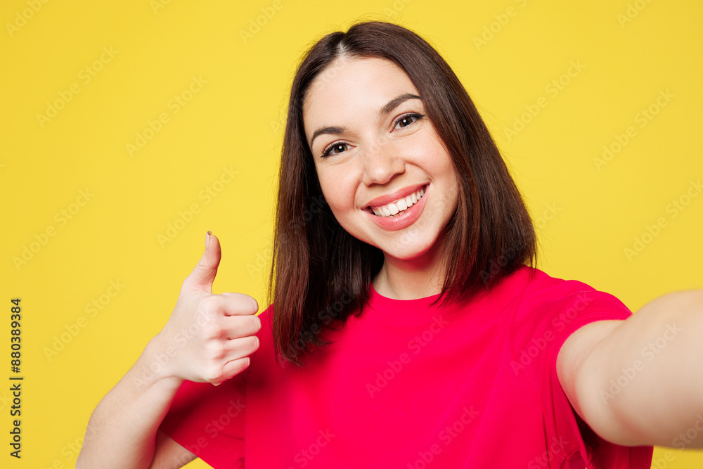 Close up young happy woman she wear pink t-shirt casual clothes doing selfie shot pov on mobile cell phone show thumb up isolated on plain yellow orange background studio portrait. Lifestyle concept. Close up young happy woman she wear pink t-shirt casual clothes doing selfie shot pov on mobile cell phone show thumb up isolated on plain yellow orange background studio portrait. Lifestyle concept.