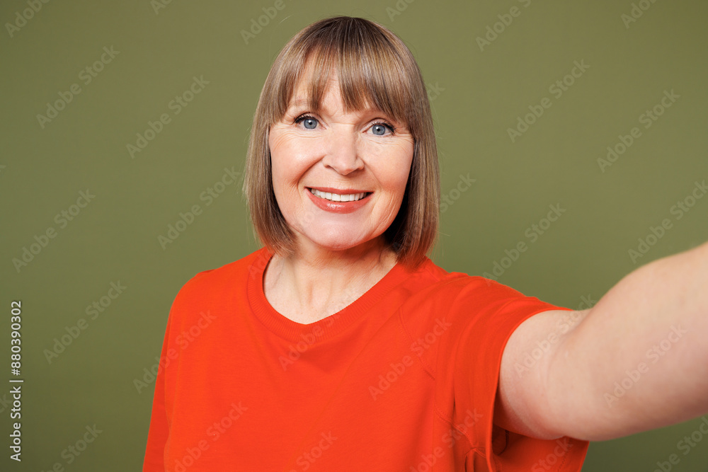 Close up elderly blonde woman 50s years old wear orange t-shirt casual clothes doing selfie shot pov on mobile cell phone isolated on plain pastel green background studio portrait. Lifestyle concept. Close up elderly blonde woman 50s years old wear orange t-shirt casual clothes doing selfie shot pov on mobile cell phone isolated on plain pastel green background studio portrait. Lifestyle concept.