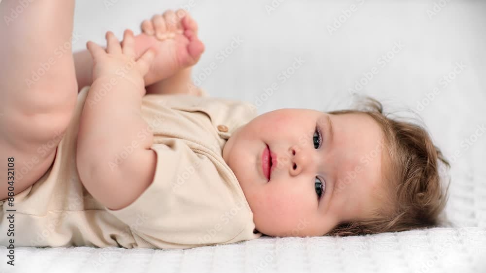 Charming baby girl of five months lying in bed face up and looking at camera, portrait of infant Charming baby girl of five months lying in bed face up and looking at camera, portrait of infant