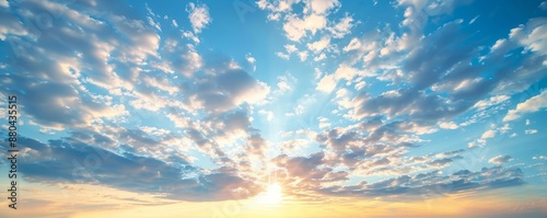 An orange sun on an orange sky with blue skies and clouds