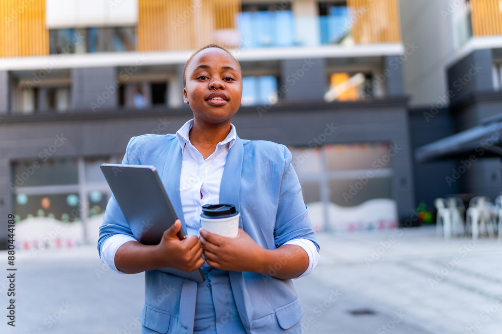 A young business woman with short cropped hair carries a laptop and coffee in her hand in front of a business building A young business woman with short cropped hair carries a laptop and coffee in her hand in front of a business building