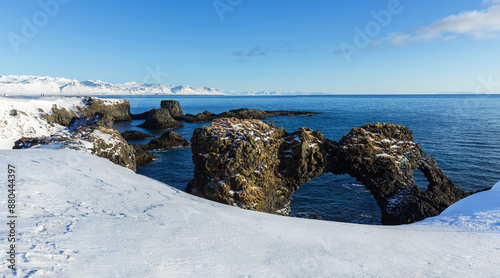 High angle view of snow covered hill above a volcanic rock Hellnar Arch with hole against sea near Gatklettur, Iceland
 photo